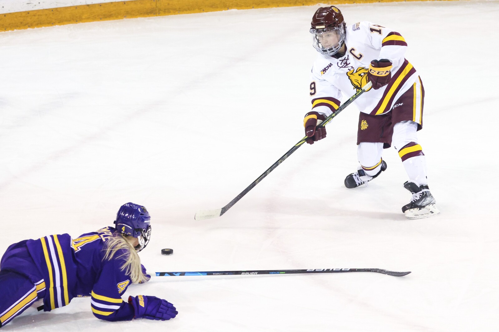 Women hockey players in purple and yellow compete against players in white and maroon at Amsoil Arena