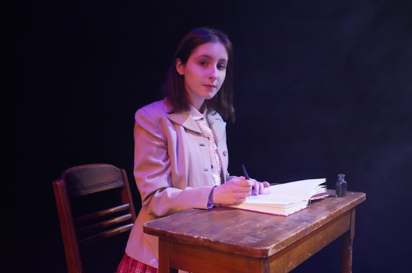 Young girl sitting at desk, writing in diary and looking thoughtful.