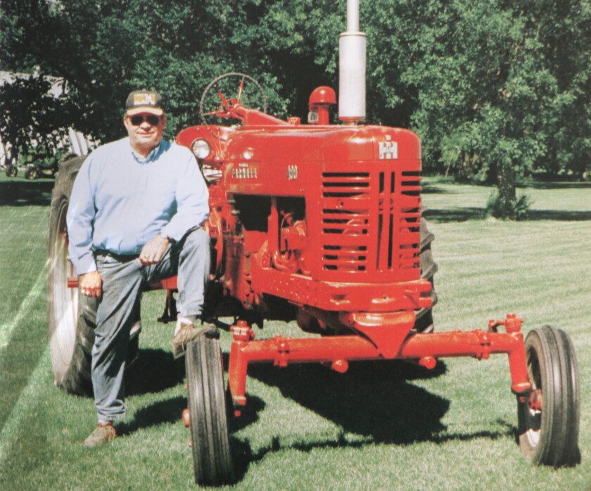 A man in a farmer cap stands next to an red, International Harvester, vintage tractor.