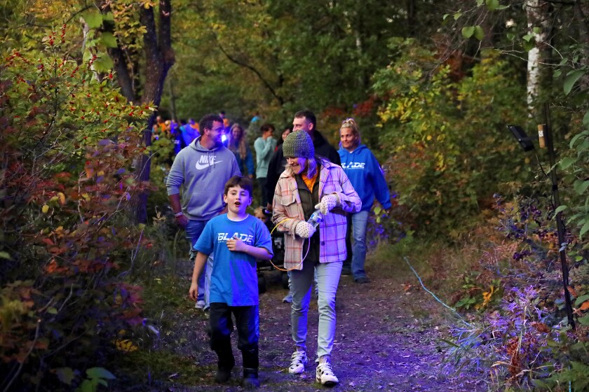 People walk through the woods at the arboretum lit by black lights.