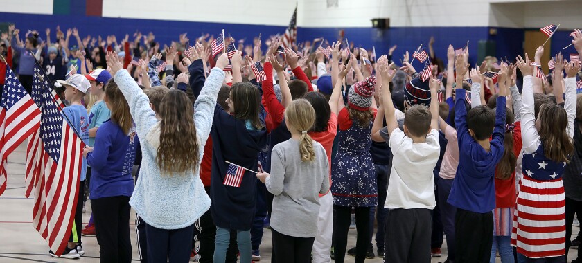 Students at Great Lakes Elementary School hold up flags as they perform a song during their Veteran’s Day ceremony