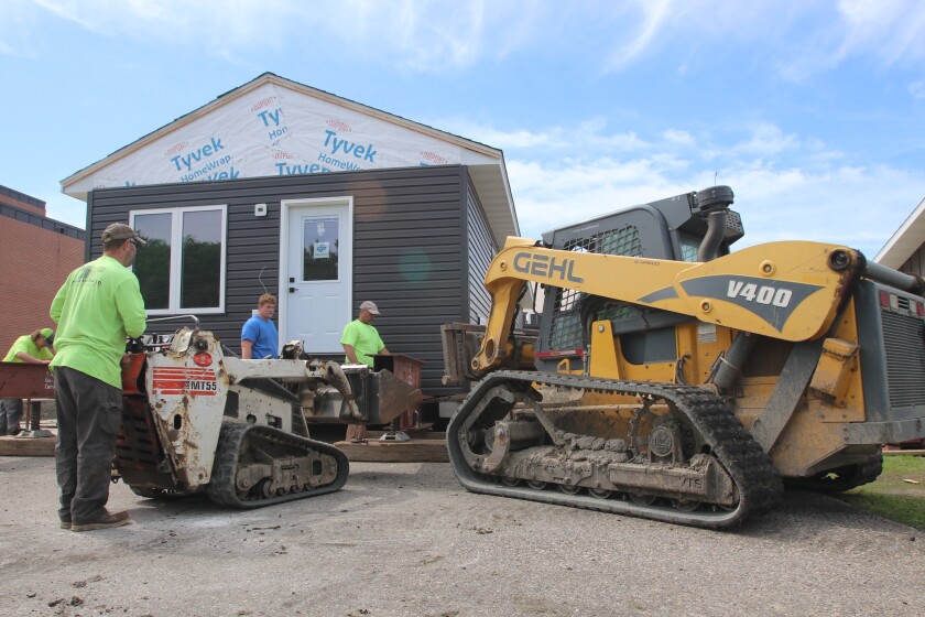 Small machinery and people bustle around a nearly complete house