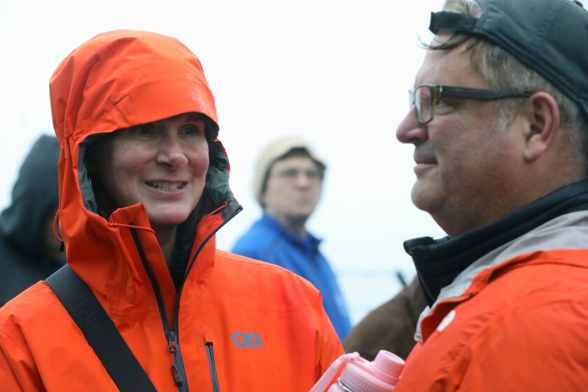 A woman wearing a raincoat talking with a man while at an outdoor ceremony.