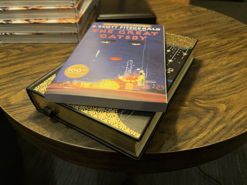 Comercialize edições de brochura e capa dura de F. Scott Fitzgerald "O Grande Gatsby" sente-se em uma mesa redonda de madeira. As bordas de outros livros são visíveis atrás.