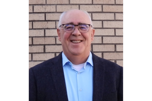 Headshot of a man standing in front of a brick wall.