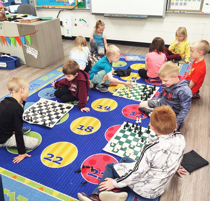 Ten kindergarten students at Parkers Prairie Elementary School sit on a blue floor mat playing chess. Students get the choice to play chess, and about half the class has learned the game.