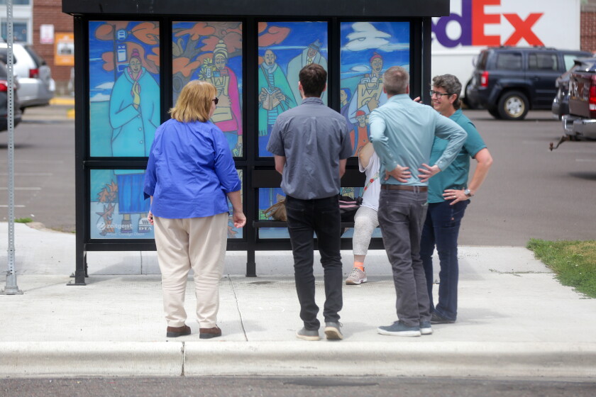 People standing and looking at a bus shelter that has a mural painted on the windows.