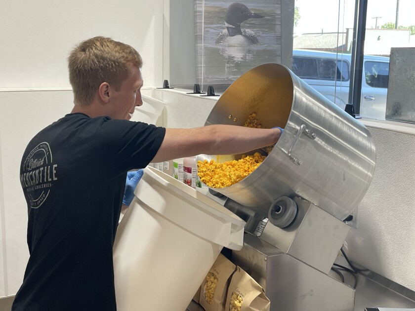A young man in a black t-shirt reaches into a silver pot full of popcorn.