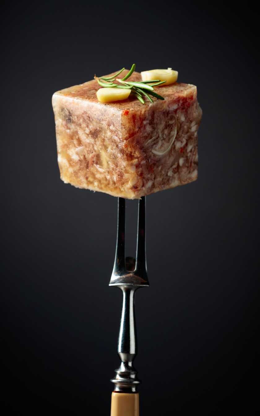 cube of gelatinous brown substance on fork, garnished with slices of garlic and rosemary sprig