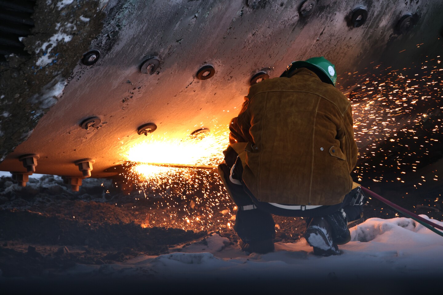 A worker uses a cutting torch to dismantle an old grinding mill