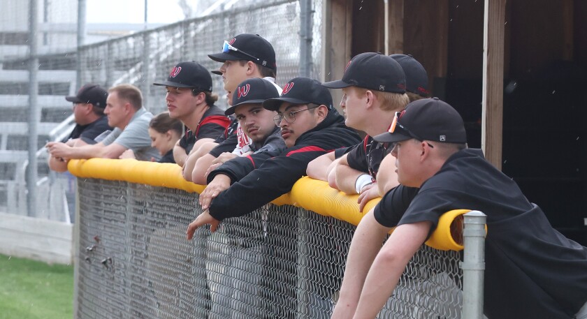 Worthington High School Activities Director Josh Dale (in gray) joins the Trojan dugout and monitors the weather on his cell phone as Severe weather starts to move into the area Wednesday evening.
