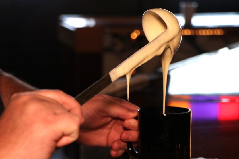 Batter drips from a ladle into a mug.