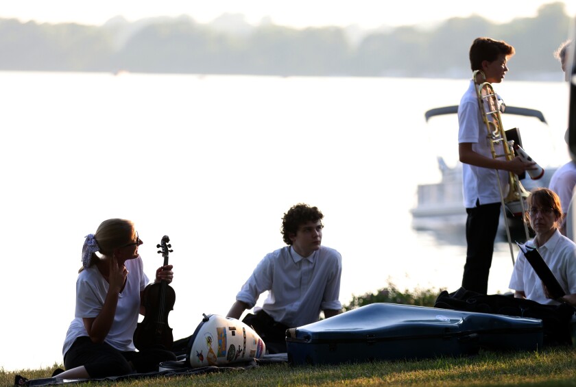 Members of the Worthington Area Symphony Orchestra wait on the shore of Lake Okabena at Chautauqua Park Monday evening before going on stage after the "Amazing" Worthington City Band.