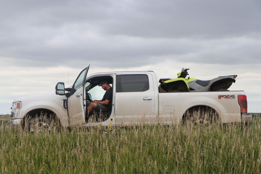 A man sits pondering a technical journal in a white pickup and yellow ATV setup, indicating he is a crop consultant.
