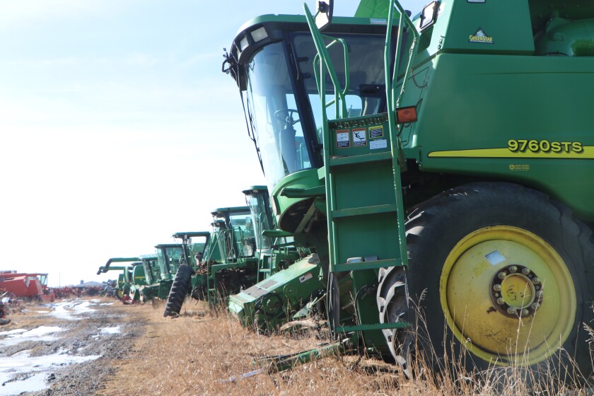 A lineup of late-model John Deere combines stand, waiting for peers in the field to break down or go off warranty, when recycled parts will go into demand.