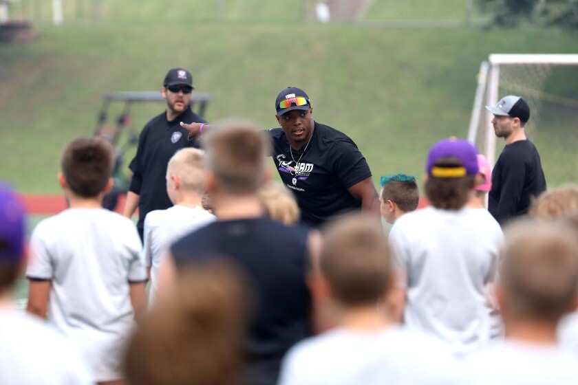 A pro football player pointing while giving instructions to kids at a youth camp.