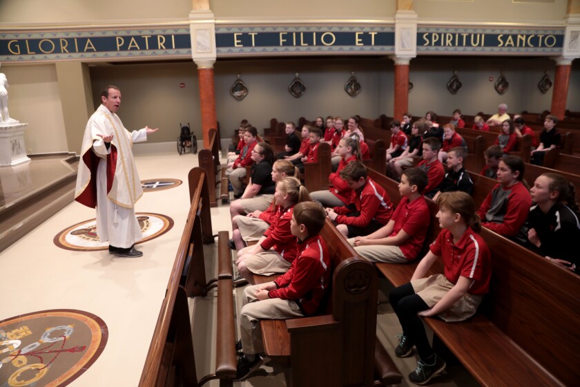 As young Titans listen with eagerness, Father Kregg Hochhalter conducts a Mass at Trinity Elementary North, which didn't exist as a normal routine in that particular school prior to his arrival.