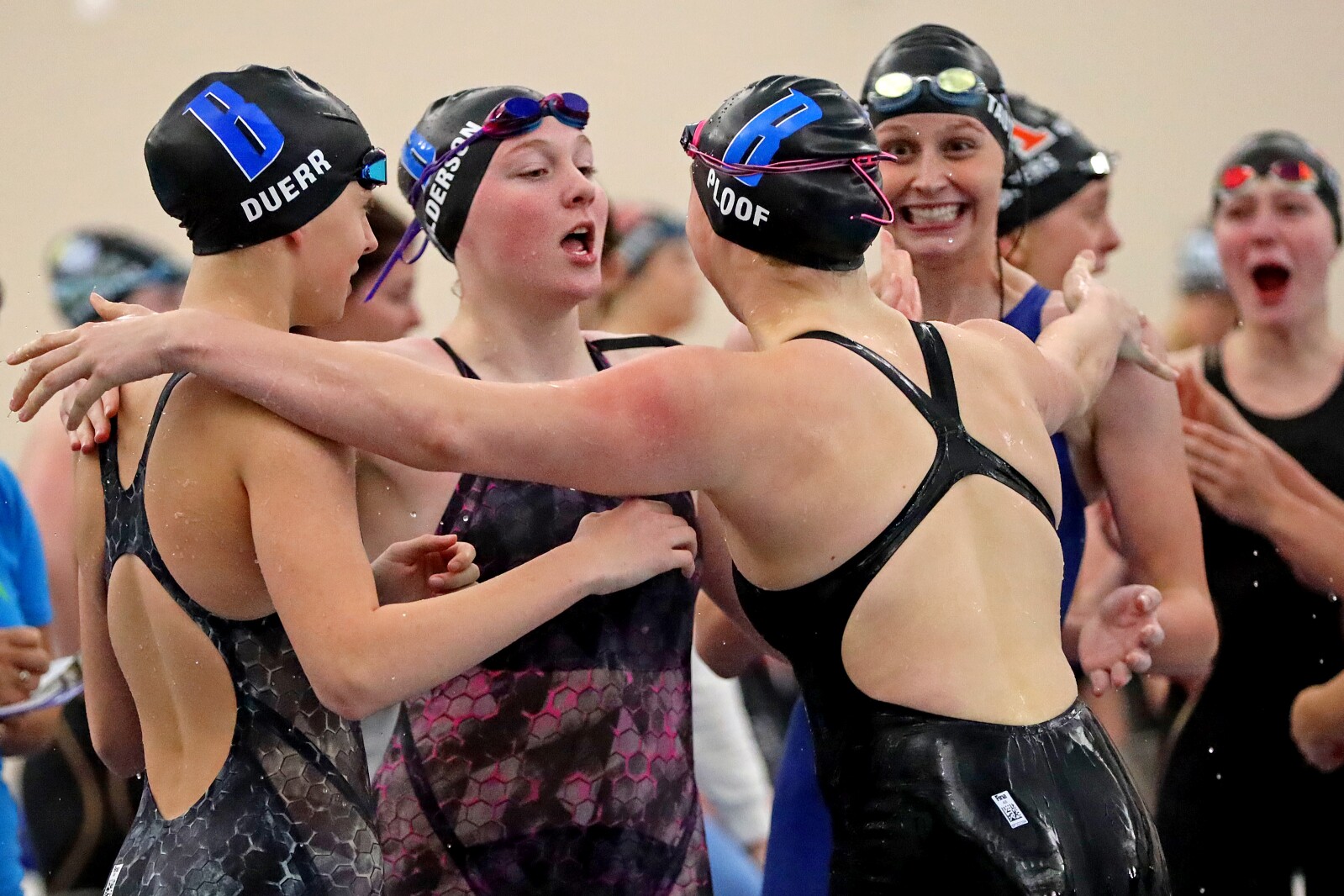 Relay swimmers embrace each other in a small group as they react happily to winning.