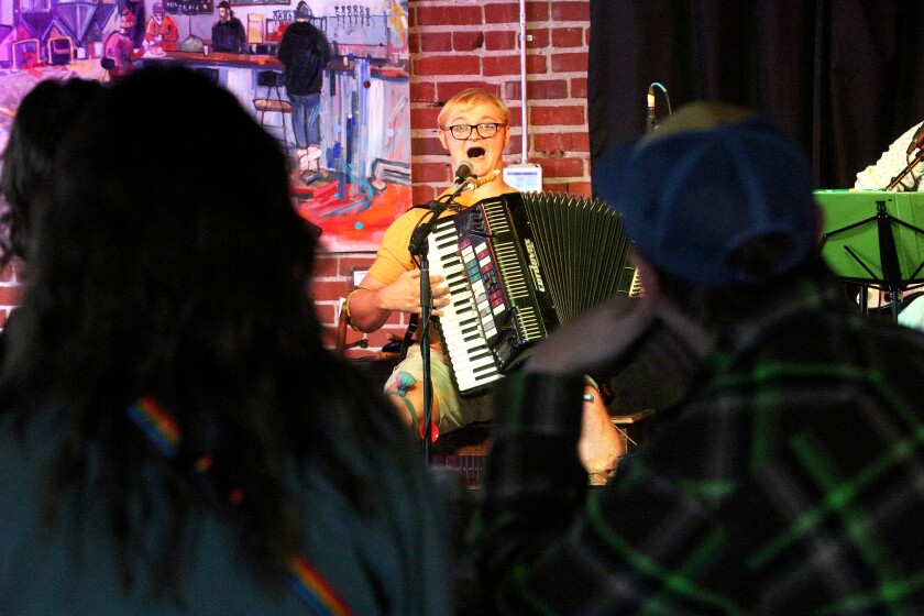 A man sings while playing an accordion as spectators watch.