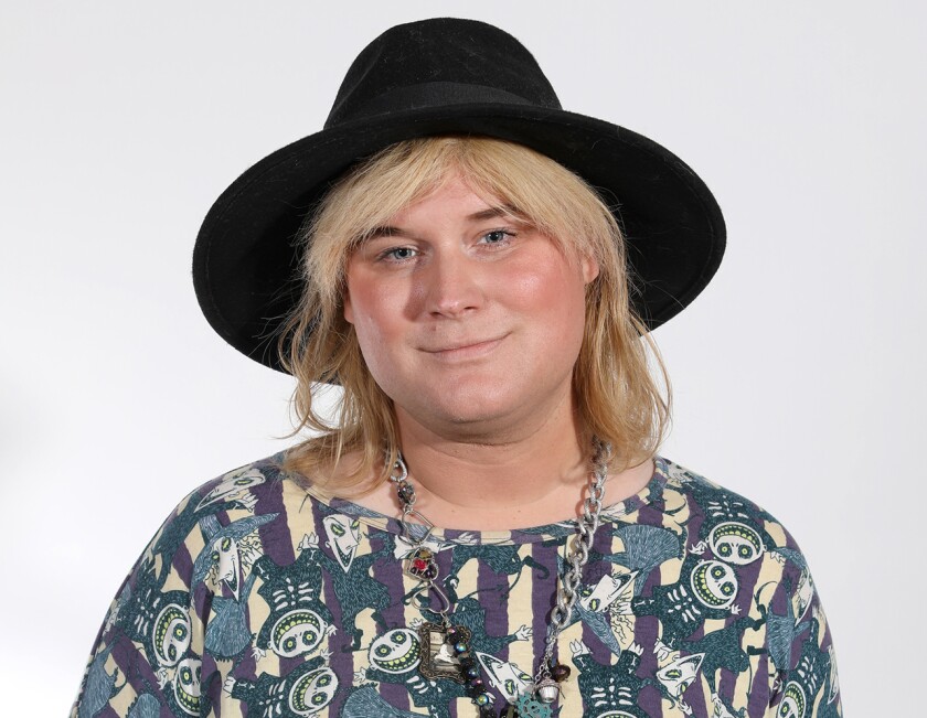 Studio portrait of blonde woman smiling slightly, wearing wide-brimmed black hat and Nightmare Before Christmas blouse.