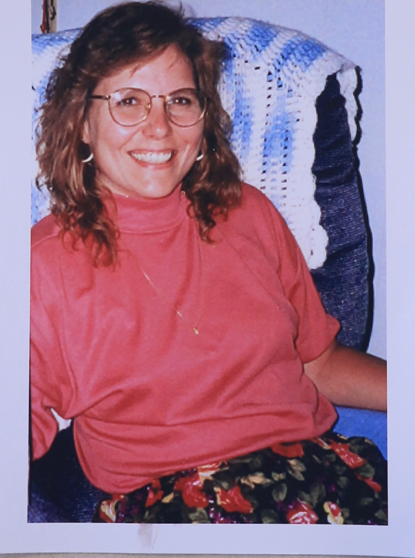 A picture of Sandra Jacobson sitting on a chair, smiling for the camera