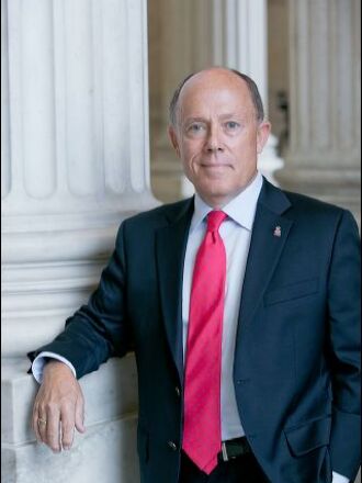 Man wearing a suit and tie stands next to a white column