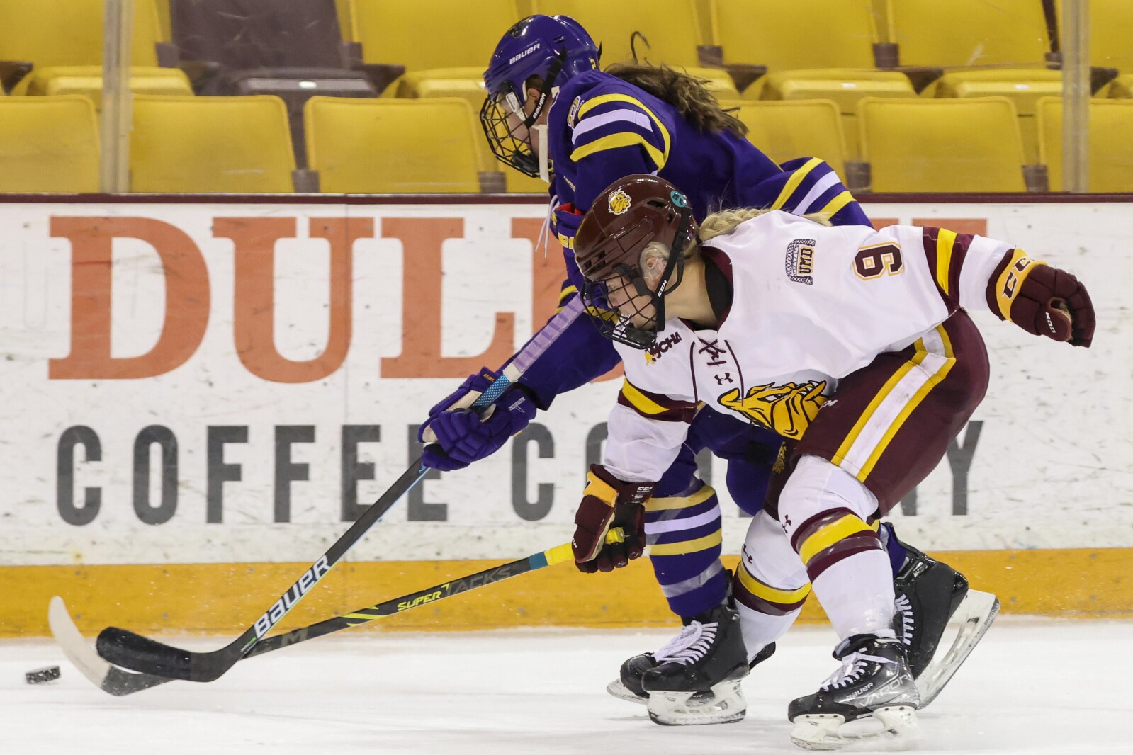 Women hockey players in purple and yellow compete against players in white and maroon at Amsoil Arena