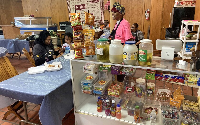 Woman smiling behind front counter while customers and colleagues sit