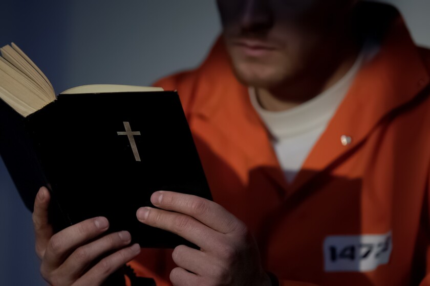 Imprisoned man in handcuffs reading bible, feeling guilty and praying for soul