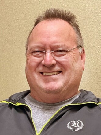 A face photo of a smiling man in a gray sweatshirt.