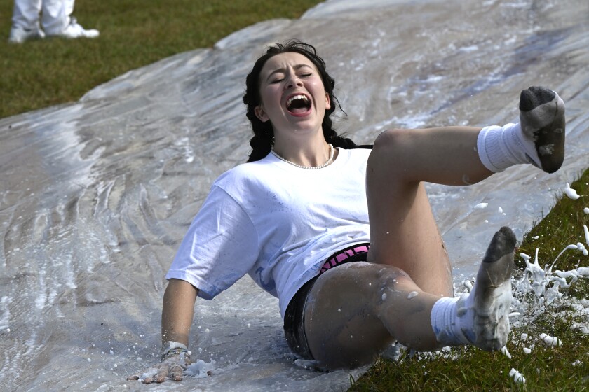 A student slides down a sheet of plastic coated with detergent and blue color dye.