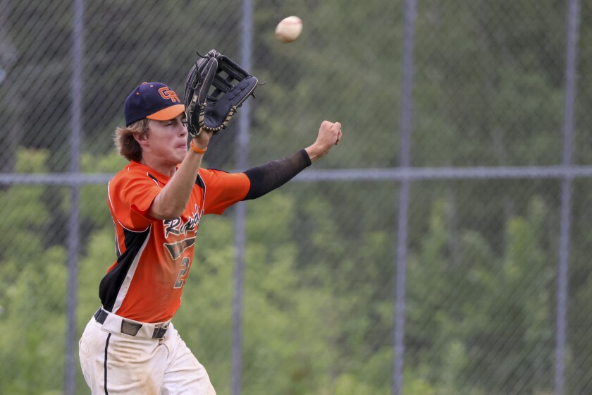boys playing baseball outside in black and orange uniform and in black and red uniforms
