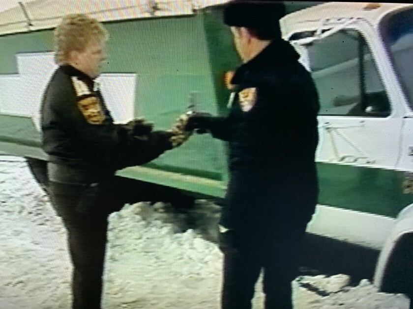 Two police officers stand in the snow near a large green truck.