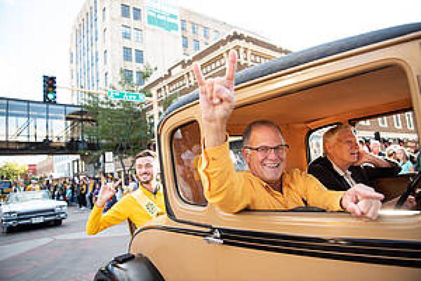 A smiling NDSU President Dean Bresciani throws "horns up" during a parade in Fargo