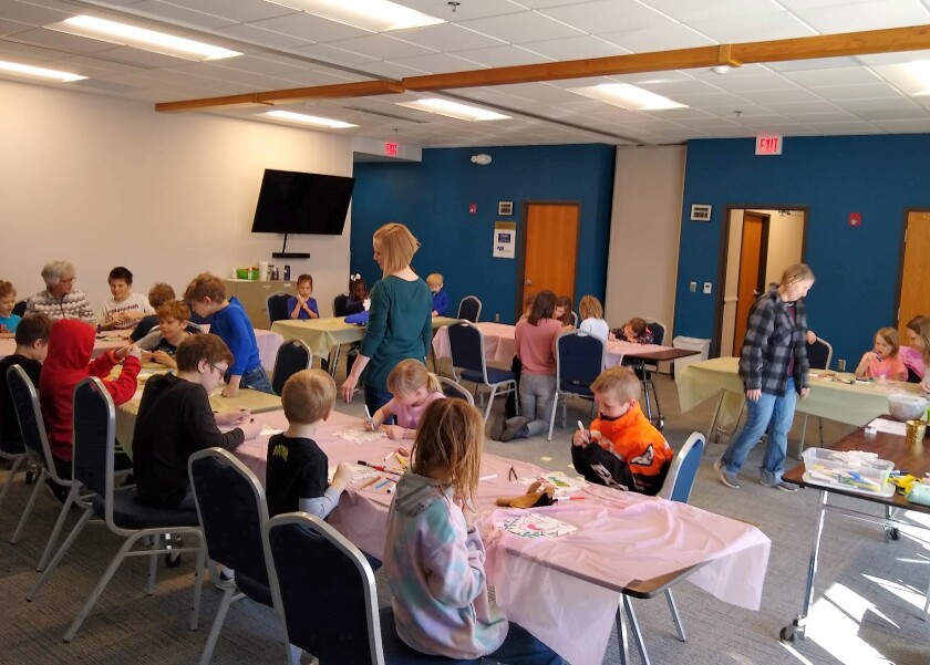 Becky Foster walks among the children as they color puzzle pieces for the mural