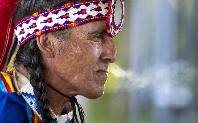 Richard Hill of Sisseton, South Dakota exhales smoke from his cigarette while waiting for the Upper Sioux Community's traditional WACIPI to begin on the evening of Friday, August 5, 2022.