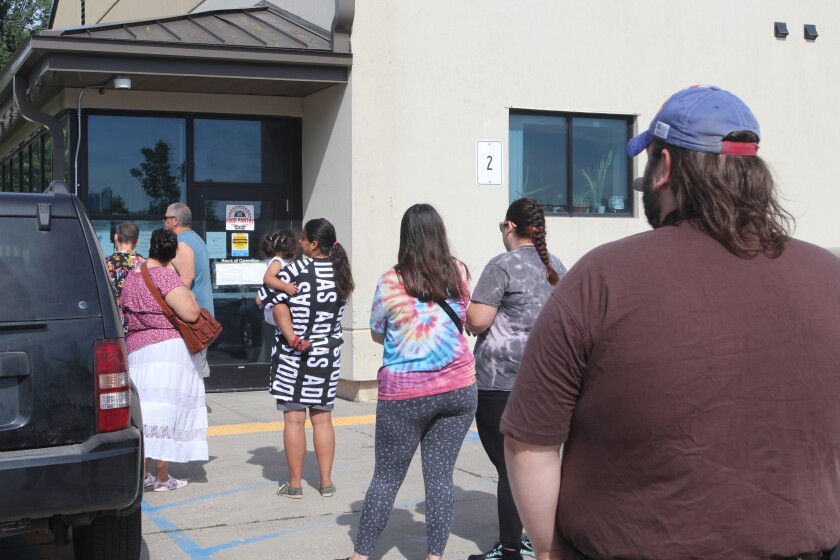 A small group, including a woman holding a toddler, wait on the pavement outside a building.