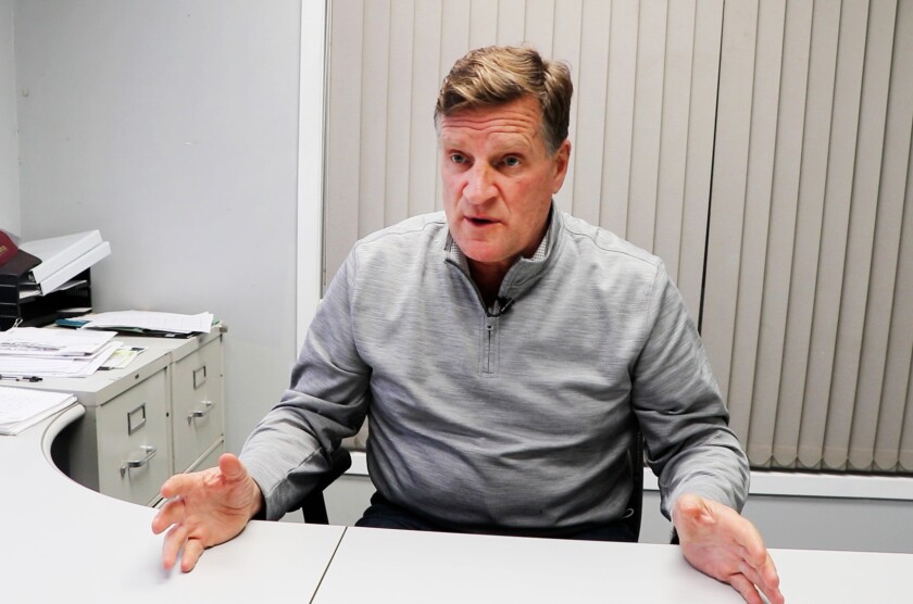 Tom Campbell, sits at an office table, gesturing with his outstretched hands. The photo was taken after he had attended the Jan. 6, 2021, rally for President Donald Trump in Washington, D.C.