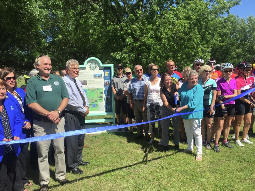 A group poses for a photo prior to cutting a ribbon for a kiosk on the Mississippi River Trail in Kiwanis Park in Brainerd Tuesday afternoon. (Brainerd Dispatch/Spenser Bickett)