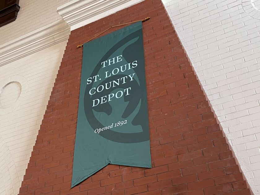 A green banner, hanging on a brick chimney against a white-painted brick wall, reads THE ST. LOUIS COUNTY DEPOT.