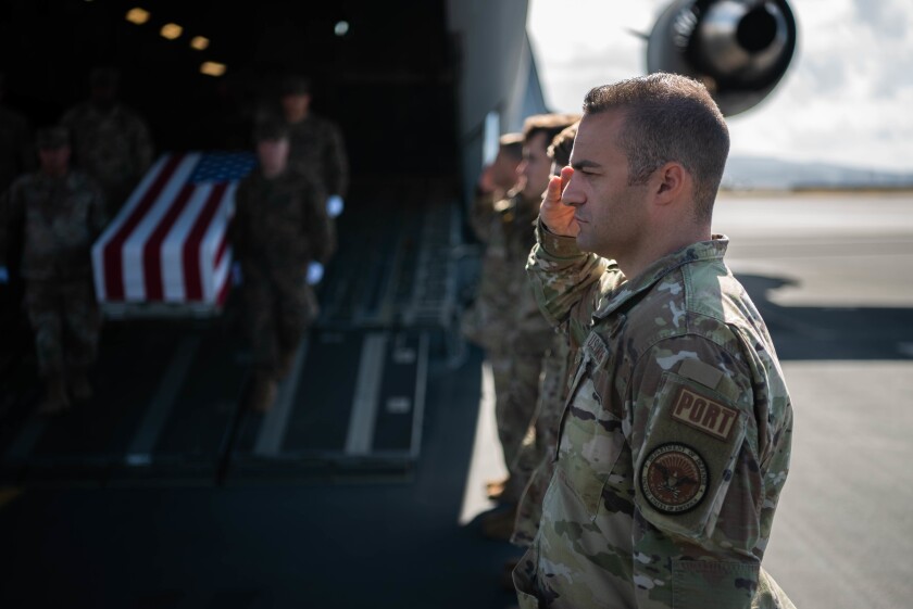 Service members salute while flag draped caskets are carried from a U.S. cargo plane.
