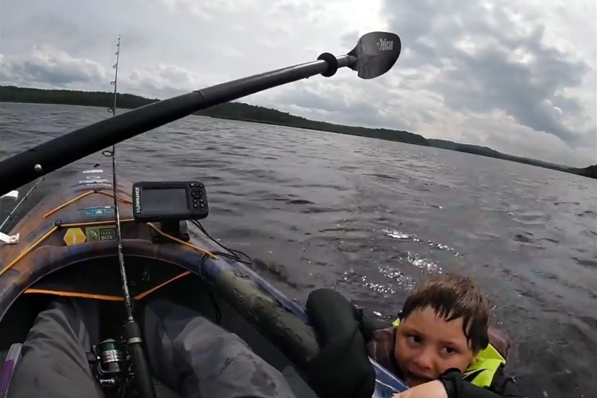 A young boy clinging to the side of a kayak