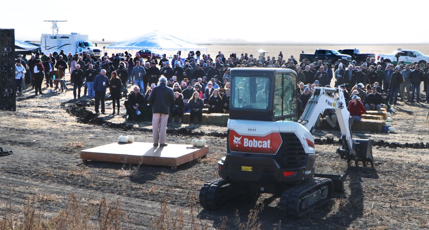 A man speaks to a farm field audience of about 300 people.