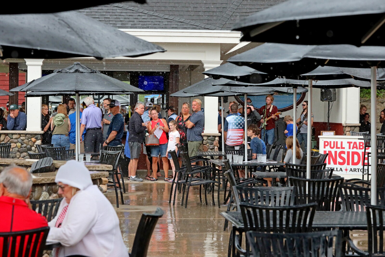 People seek shelter under a table umbrella and next to the building from a sudden rain shower.