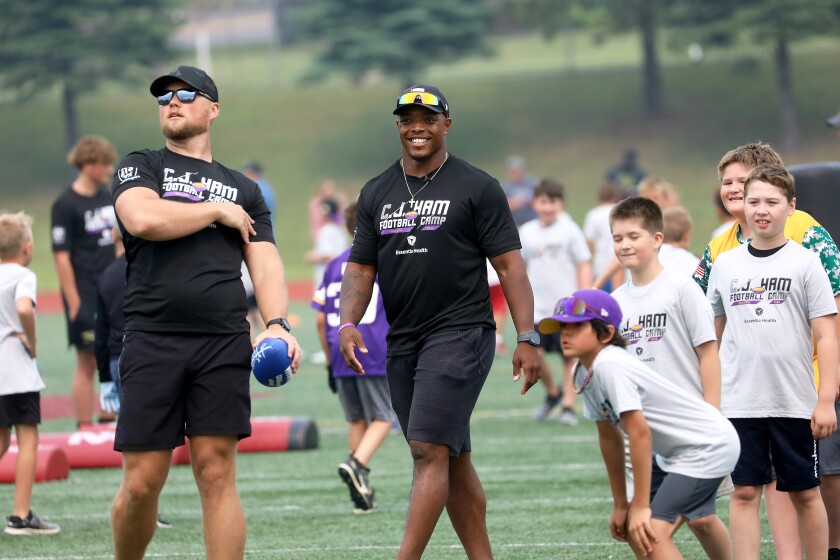 A pro football player smiling while watching drills at a youth camp.