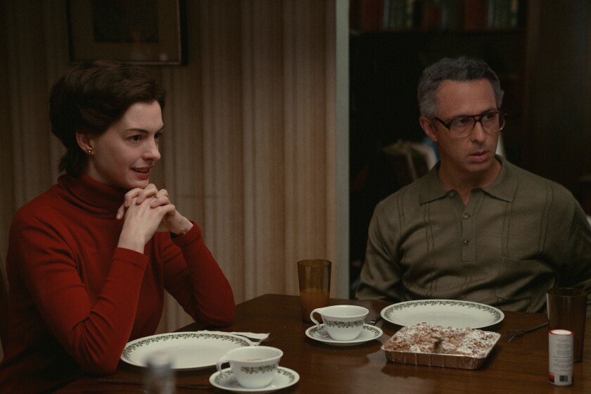 Light-skinned woman and man sitting at a dining table set for a meal. They are both looking towards the right, as if in conversation.