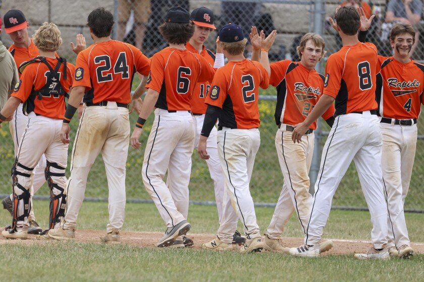 boys playing baseball outside in black and orange uniform and in black and red uniforms