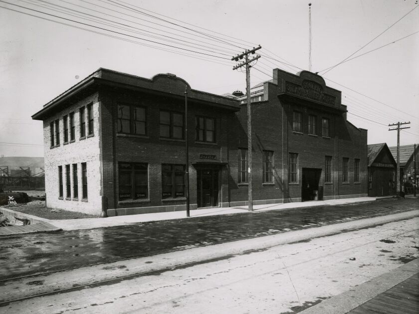 A black-and-white image of a large brick building on an empty city street.