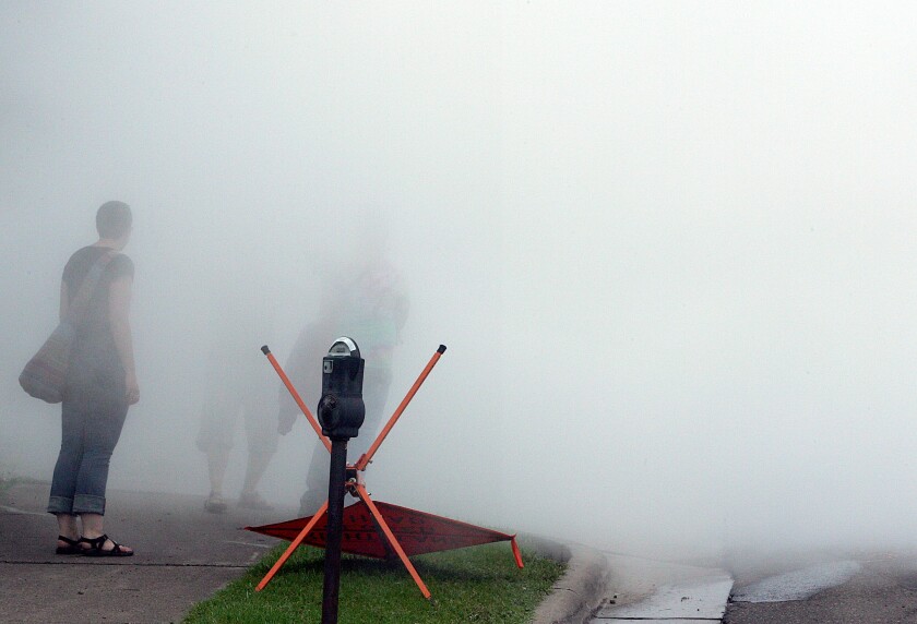 Outlines of people are seen through steam next to a parking meter and a fallen sign
