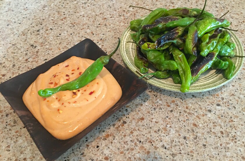 plate of orange dip with whole green pepper on top and plate of roasted green peppers